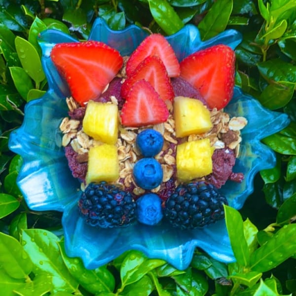 A Big Island Bowls acai bowl with strawberries, pineapple, blueberries, and blackberries in a blue bowl.