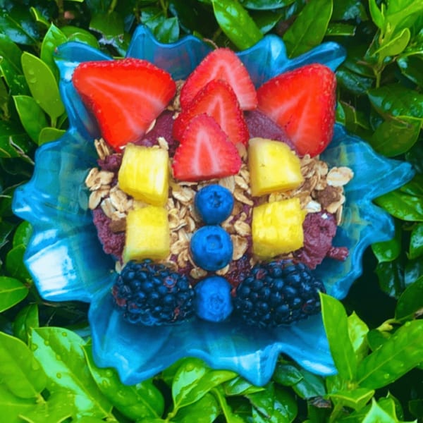 A Big Island Bowls acai bowl in a blue dish, topped with strawberries, pineapple, blueberries, and blackberries.