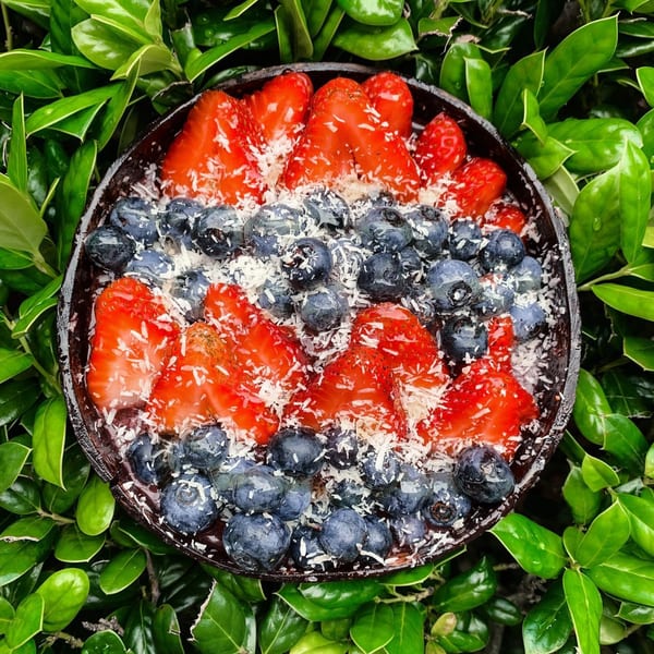 Big Island Bowls' acai bowl with strawberries, blueberries, and shredded coconut, surrounded by green leaves.