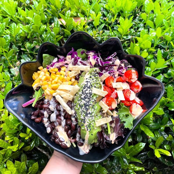 A colorful Big Island Bowls salad with corn, black beans, avocado, tomatoes, and purple cabbage.